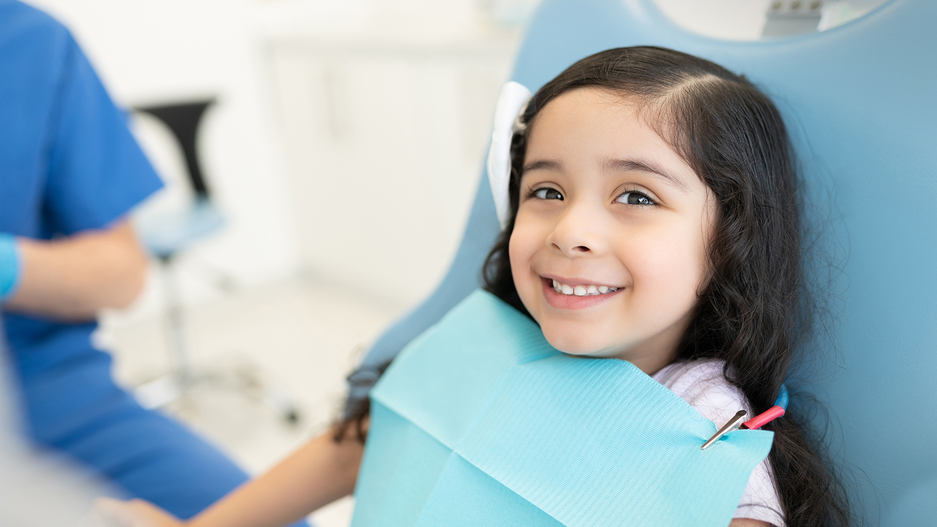 Smiling cute Hispanic girl sitting on chair at dental clinic