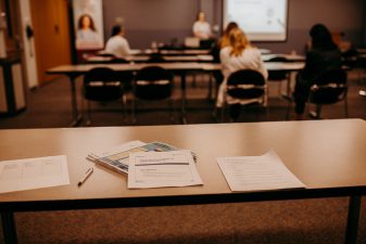 Project firstline training materials sit on a table with participants out of focus in background.